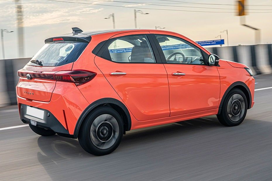 Tata Tiago in orange driving on a highway, seen from the rear right