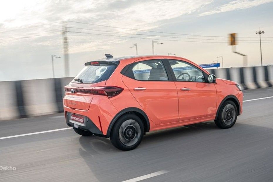 Tata Tiago in orange driving on a highway, seen from the rear three-quarter