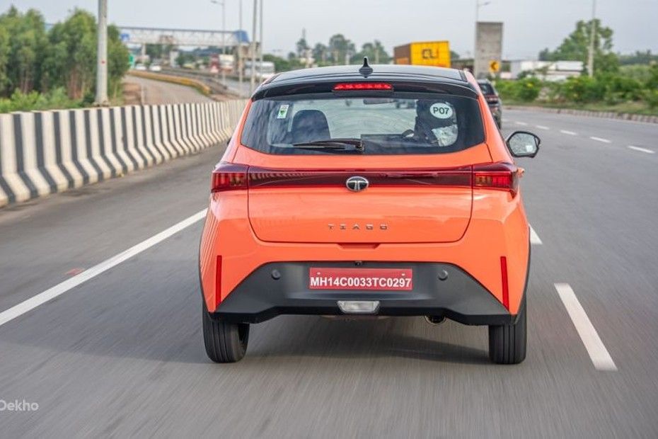Tata Tiago in orange driving on a highway, seen from directly behind
