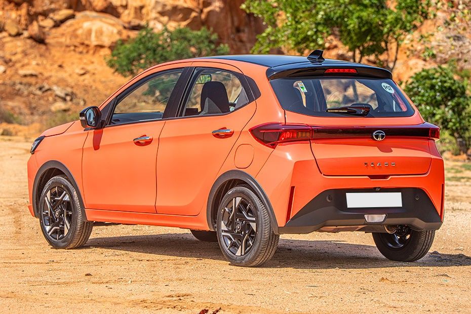 Tata Tiago in orange with black roof, rear left three-quarter view on dirt