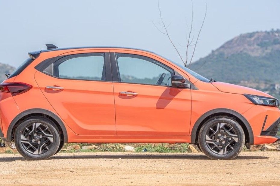 Tata Tiago in orange, side profile with dual-tone alloy wheels on dirt road