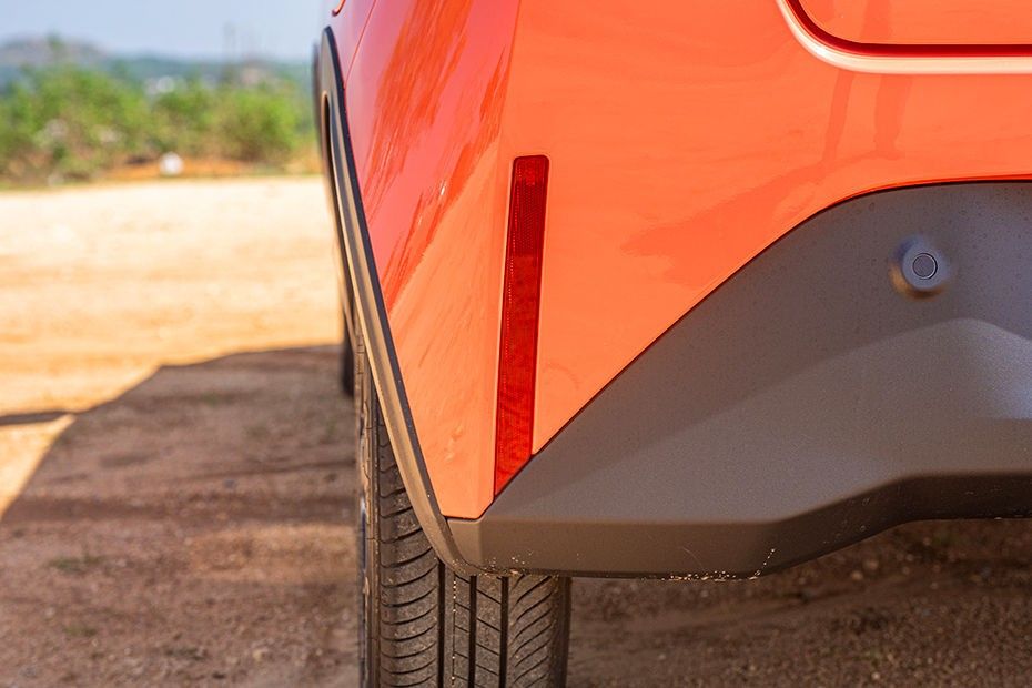 Tata Tiago rear bumper corner with red reflector and parking sensor, orange body